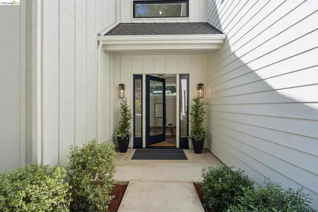 Exterior featuring white board and batten siding, white horizontal siding, a dark paneled entry door with glass inserts, and black exterior sconces Exterior featuring white board and batten siding, white horizontal siding, a dark paneled entry door with glass inserts, and black exterior sconces