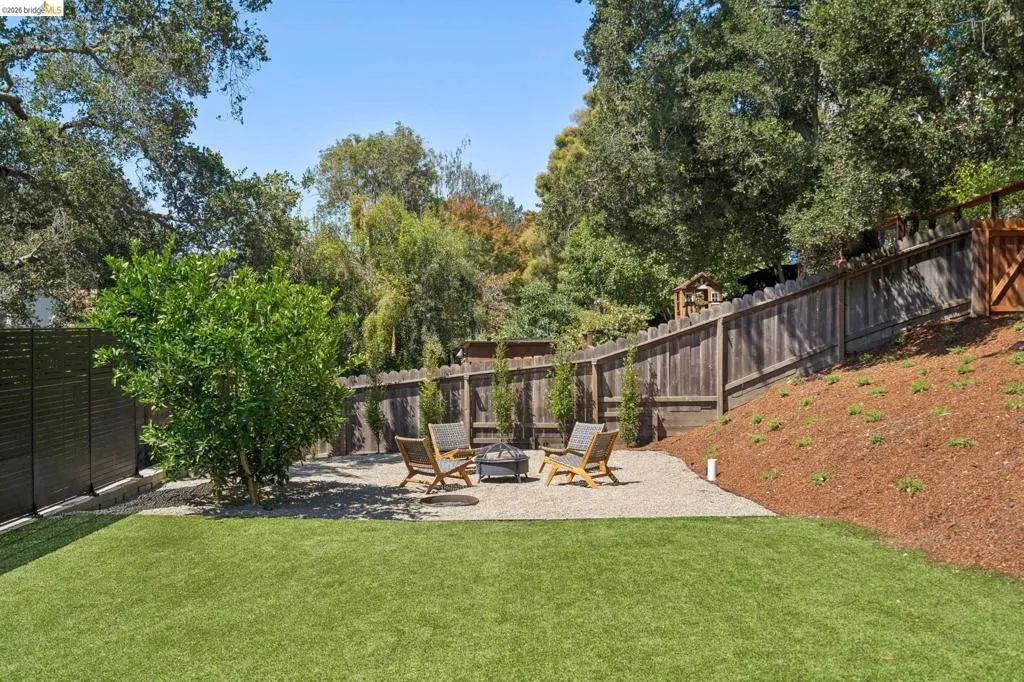 Expansive backyard featuring artificial turf, a gravel patio with a fire pit, and a terraced hillside Expansive backyard featuring artificial turf, a gravel patio with a fire pit, and a terraced hillside