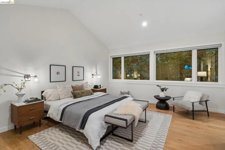 Vaulted ceiling, recessed lighting, expansive windows, wood-finish flooring, and wall-mounted sconces