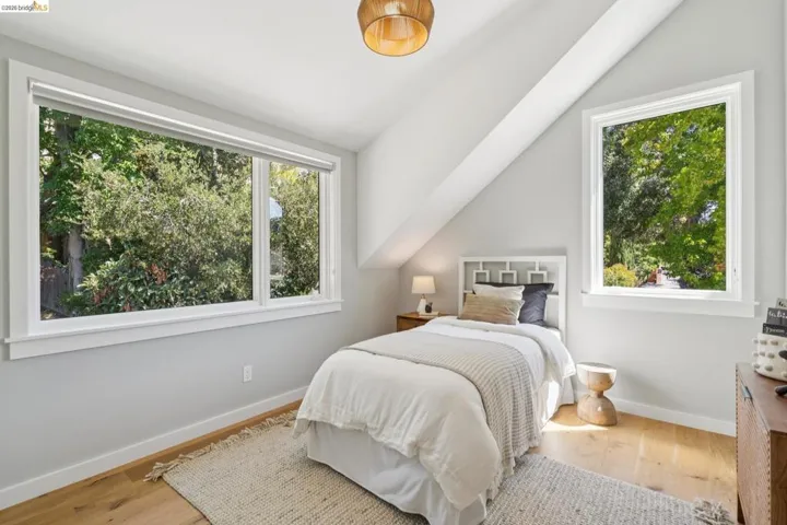 Hardwood flooring, light gray wall finish, angled ceiling, two windows, and a ceiling-mounted light fixture