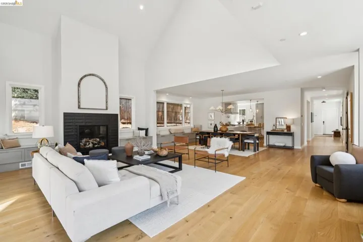 Vaulted ceilings with recessed lighting, a fireplace with a textured surround, light wood-finish flooring, and multiple windows