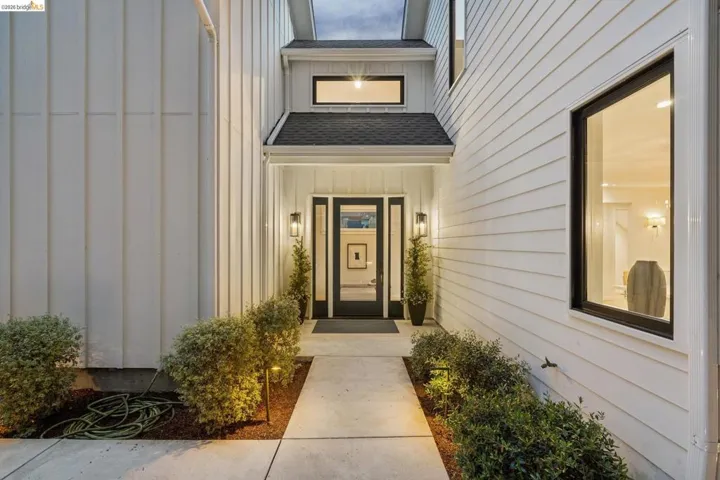 Entryway with a covered porch, transom window, dual sidelights, wall sconces, and exterior lighting