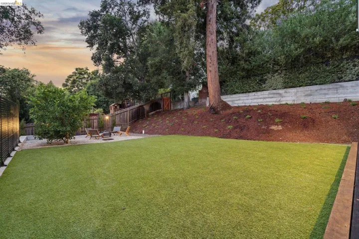 Expansive artificial turf lawn, gravel patio area, wood fencing, retaining wall, and mature landscaping