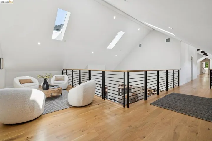 Vaulted ceiling with skylights, light wood-finish flooring, recessed lighting, and a modern horizontal railing with a wood-finish top