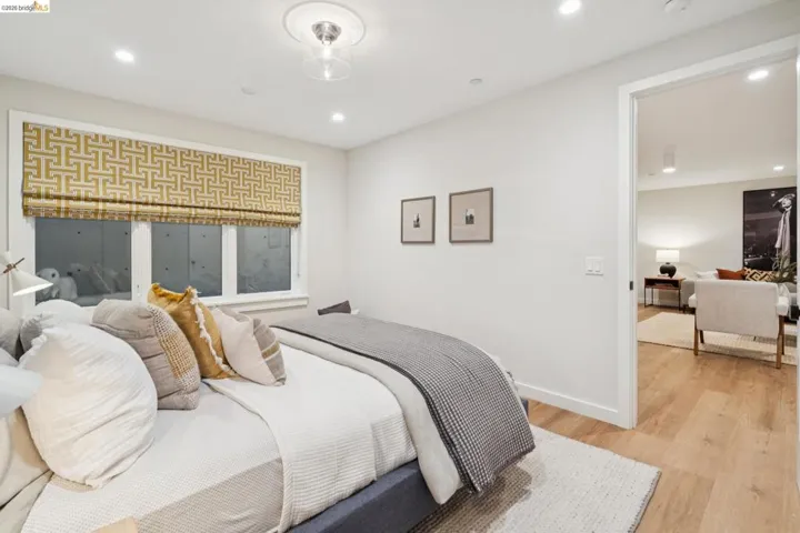 Recessed lighting, wood-finish flooring, white walls, and a patterned Roman shade