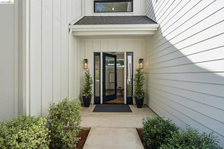 Exterior featuring white board and batten siding, white horizontal siding, a dark paneled entry door with glass inserts, and black exterior sconces