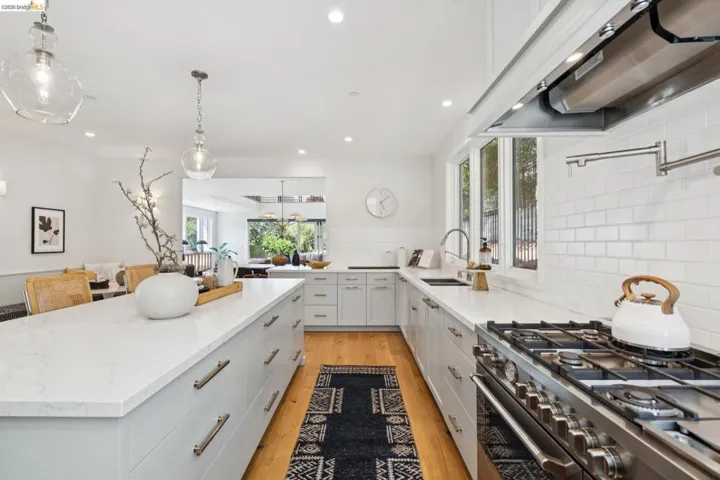 Spacious kitchen featuring a large central island, white shaker cabinetry, white subway tile backsplash, and stainless steel range with overhead hood