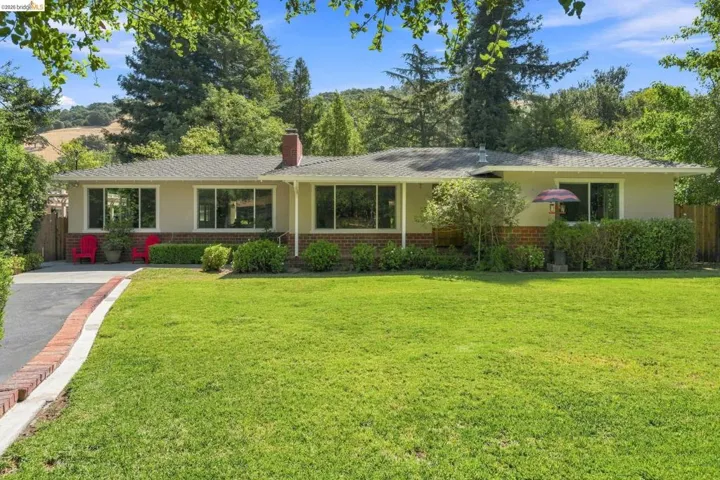 Ranch-style exterior with a brick skirt and chimney, a wide front lawn, and mature landscaping