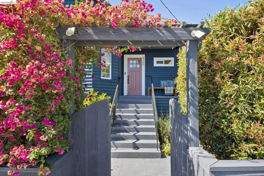 Entryway featuring a dark wood pergola, vibrant bougainvillea, and a dark wood privacy fence