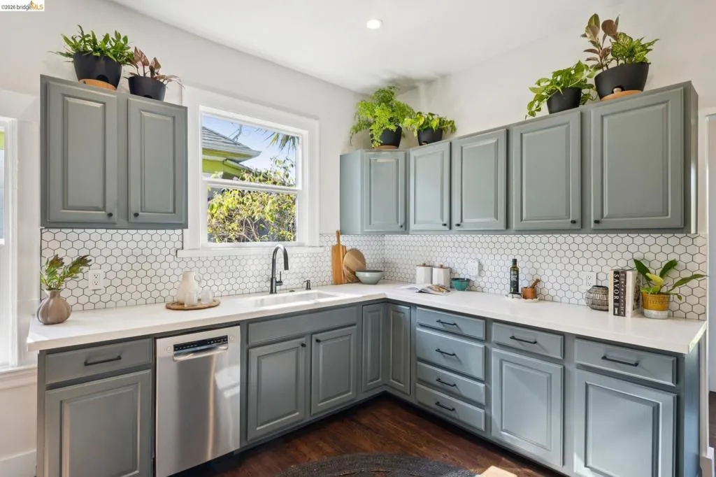 Kitchen featuring gray shaker-style cabinetry, white countertops, a white hexagonal tile backsplash, a stainless steel dishwasher, and a single-basin sink with a matte black faucet