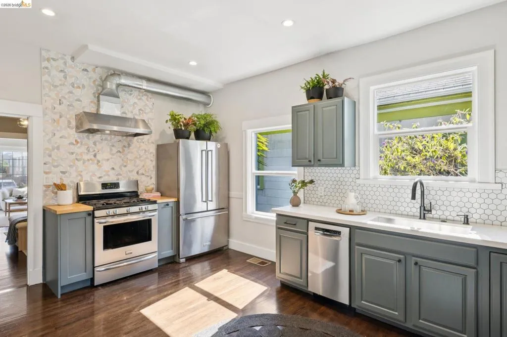 Kitchen featuring stainless steel appliances, grey cabinetry, white hexagonal tile backsplash, and dark wood-finish flooring