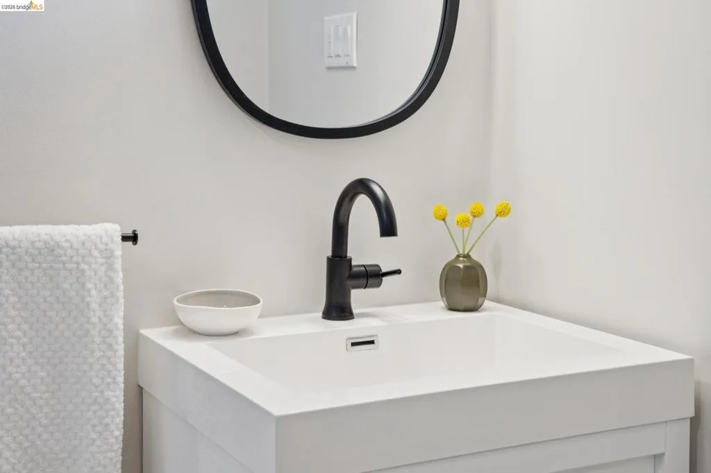 White vanity with integrated sink, matte black faucet, and a circular mirror