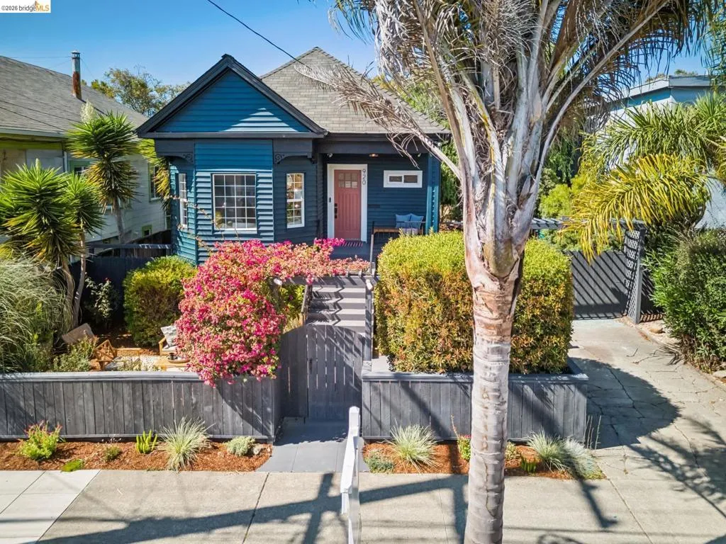Blue exterior siding with white trim, a pink entry door, a prominent front gable, and a tiered landscaped front yard with a dark fence