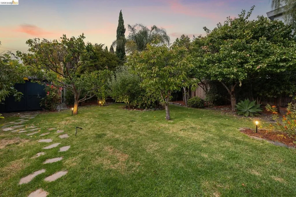 Manicured lawn with mature trees, stone paver pathway, and garden lighting