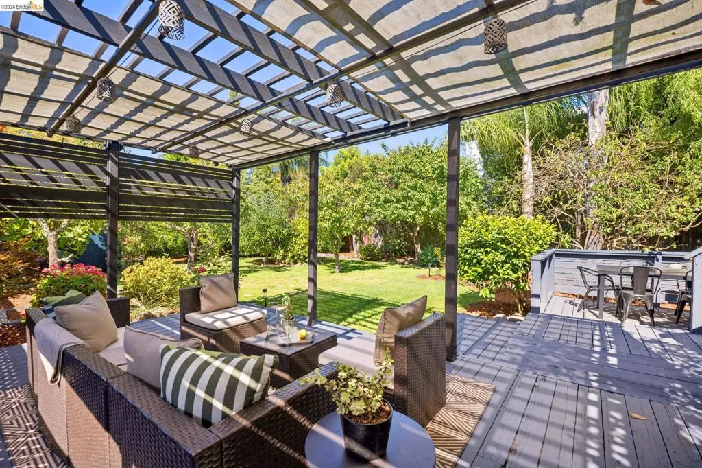 Expansive outdoor deck featuring a slat pergola with a canvas covering, integrated privacy screens, and a lush green lawn