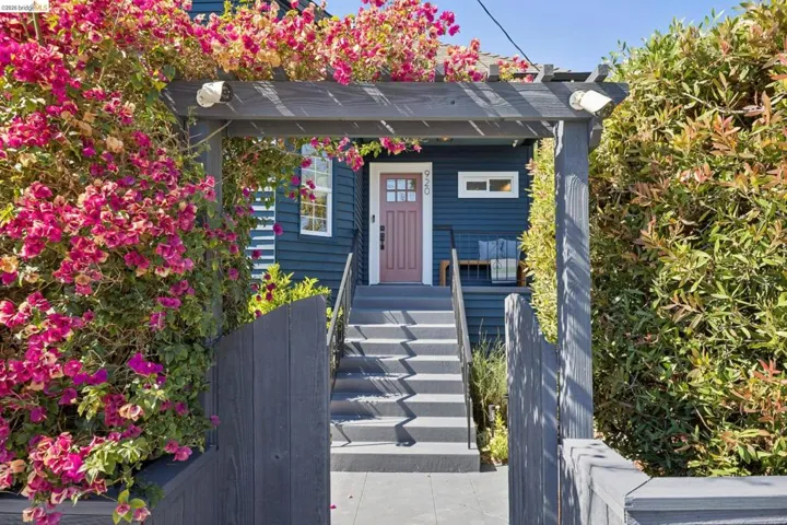 Entryway featuring a dark wood pergola, vibrant bougainvillea, and a dark wood privacy fence