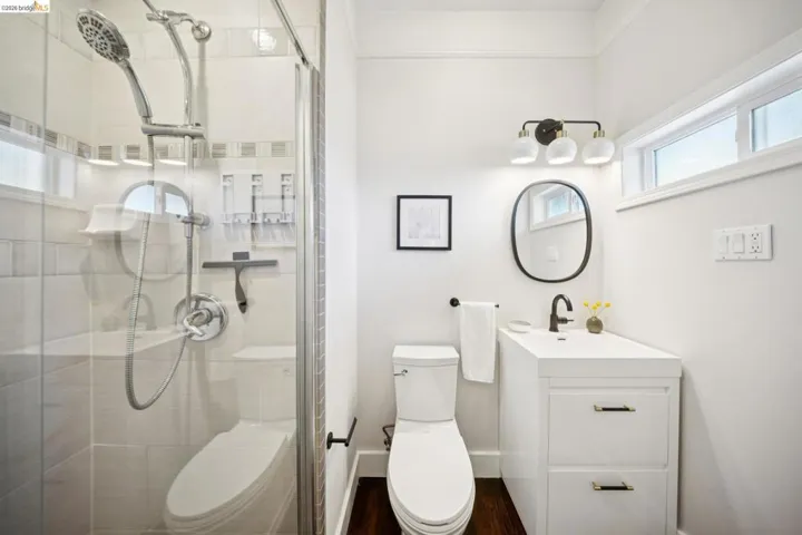 Glass-enclosed shower with tile surround, modern vanity with integrated sink, black-finish fixtures, and wood-finish flooring