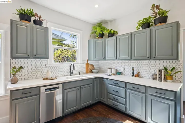 Kitchen featuring gray shaker-style cabinetry, white countertops, a white hexagonal tile backsplash, a stainless steel dishwasher, and a single-basin sink with a matte black faucet