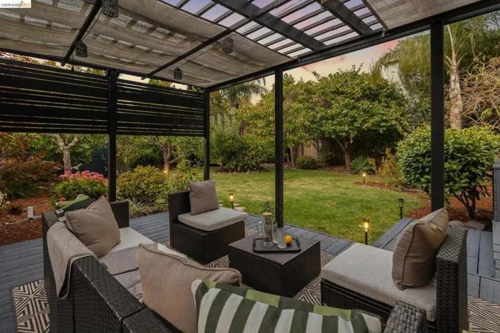 Covered outdoor patio featuring slatted privacy screens, an expansive grass lawn, and mature landscaping