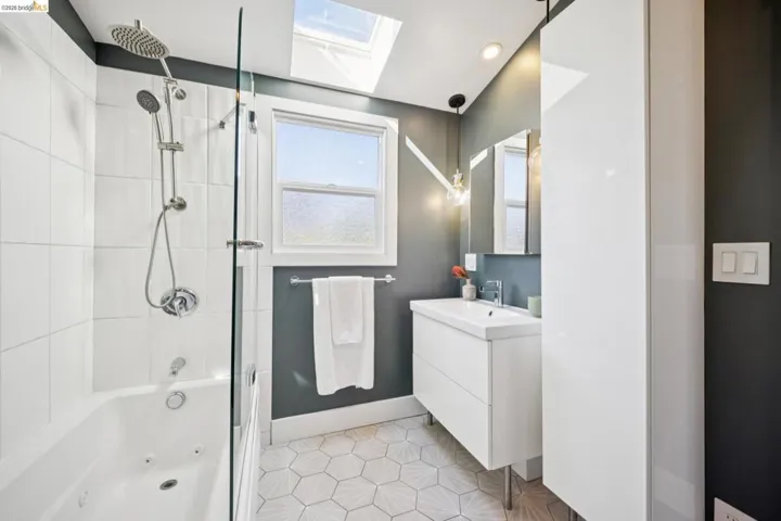 Bathroom featuring a white soaking tub with a glass shower enclosure, a skylight, and a vanity with an integrated sink