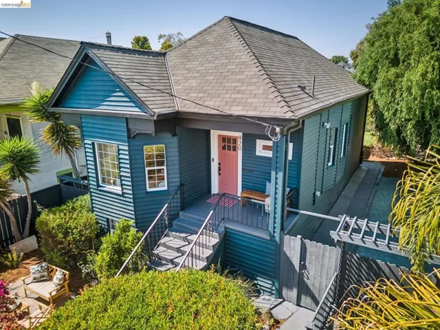 Exterior featuring blue siding, a peaked gable, a front porch with dark railings, a light wood bench, and a privacy fence