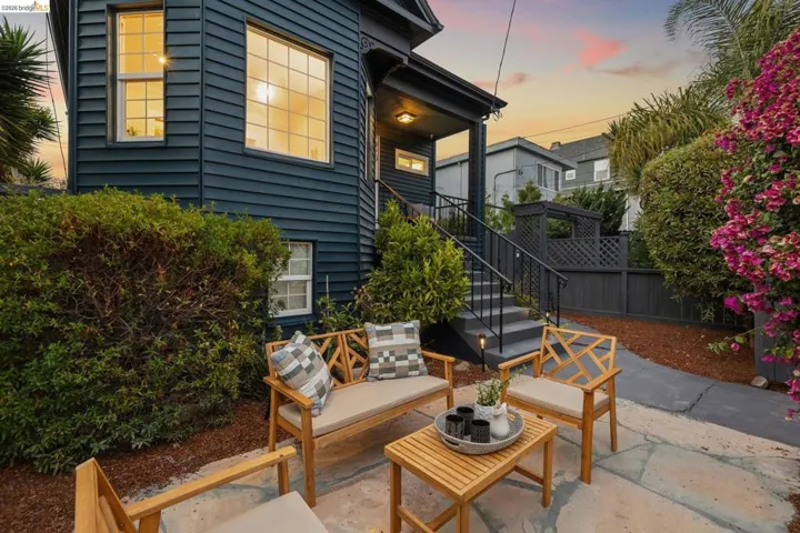 Clapboard siding exterior, elevated entry with staircase, stone patio, manicured shrubs, and mature flowering plants