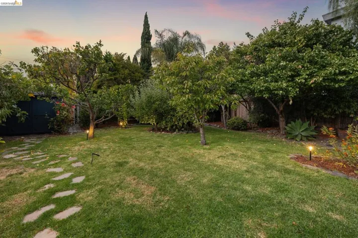 Manicured lawn with mature trees, stone paver pathway, and garden lighting