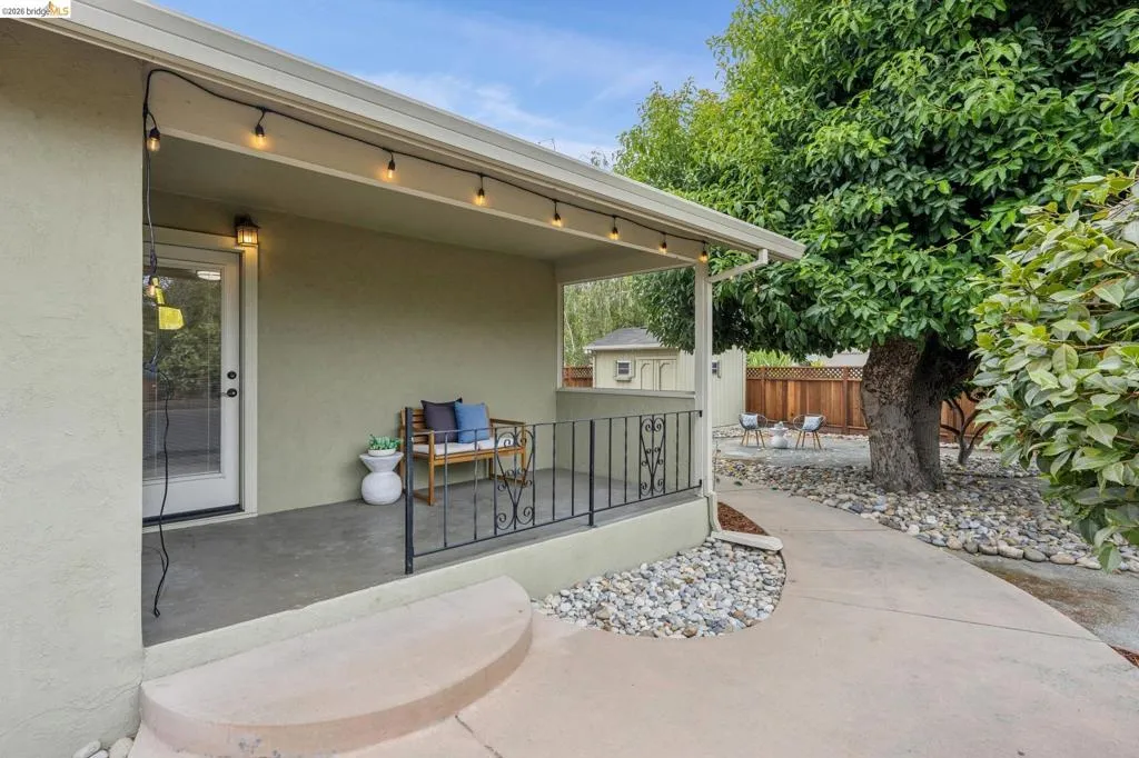 Covered patio with string lighting, direct exterior access, and a concrete pathway leading to a landscaped area
