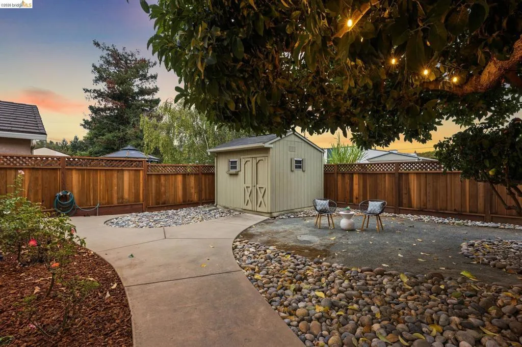 Private backyard with a wood fence, concrete pathway, and a detached shed