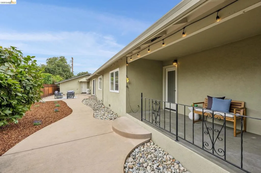 Covered patio with iron railings, stucco exterior, string lighting, and concrete walkway