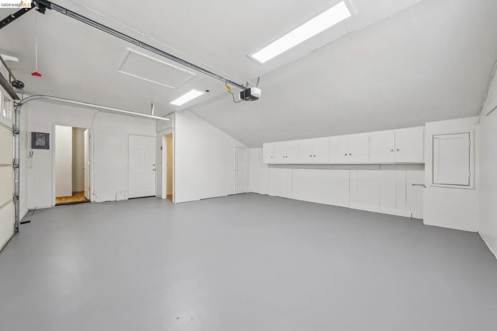 Spacious garage featuring a light gray floor, white walls, built-in white cabinetry, and overhead fluorescent lighting