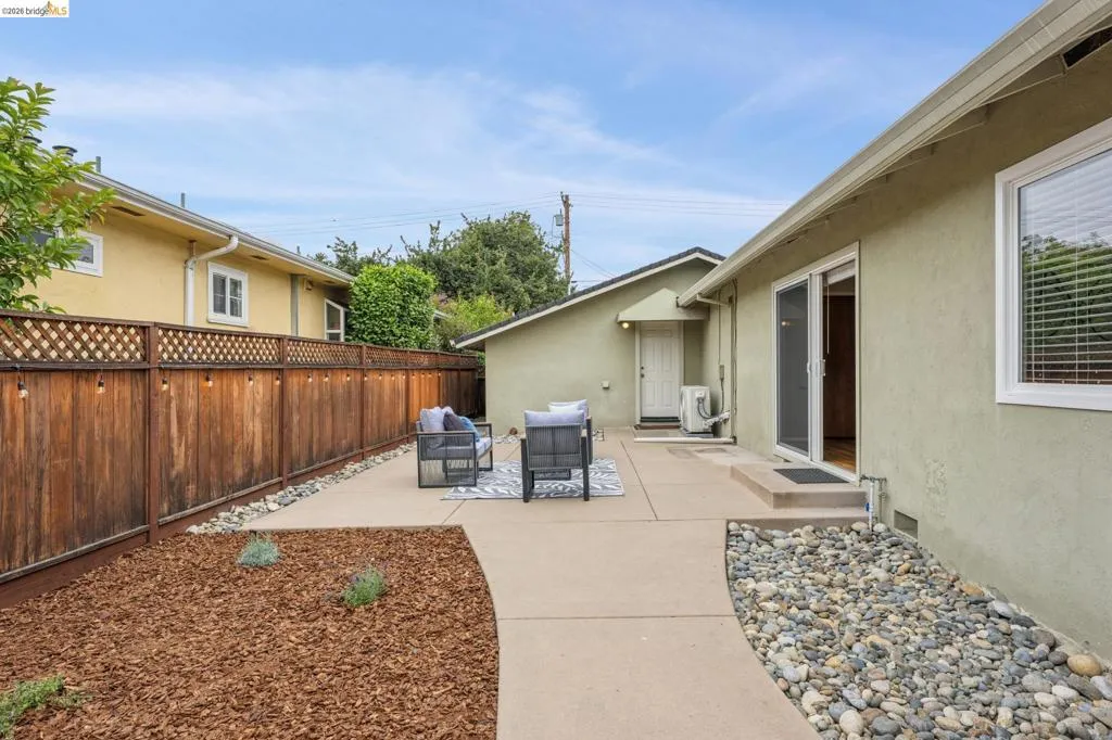 Patio area featuring concrete paving, sliding glass door access, wood privacy fencing with lattice detail, and a decorative rock border