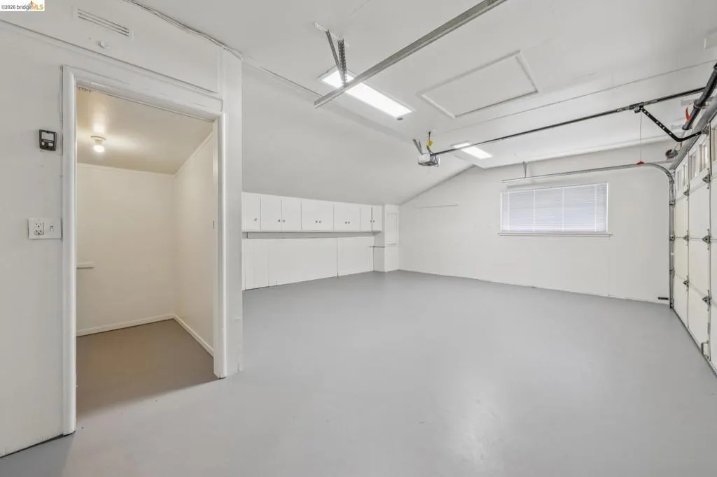 Spacious garage with built-in cabinetry, durable flooring, multiple overhead lights, and a window for natural light