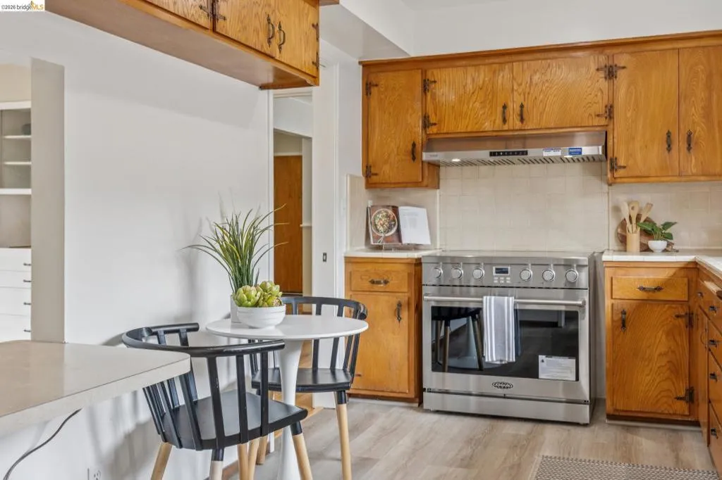 Kitchen featuring wood-finish cabinetry, a stainless steel range with a coordinating range hood, light-toned countertops, and wood-finish flooring