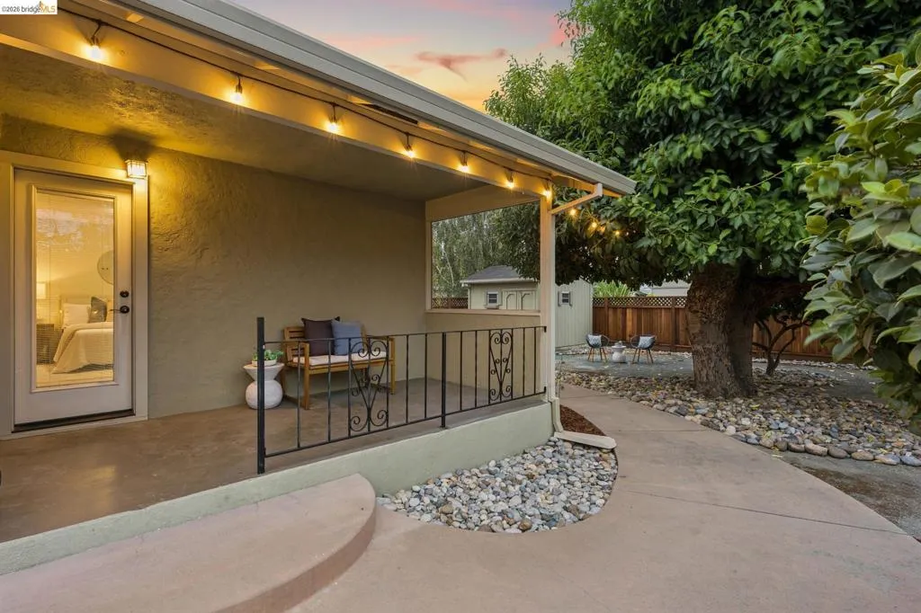 Covered patio with integrated lighting, concrete walkway, and a landscaped rock garden