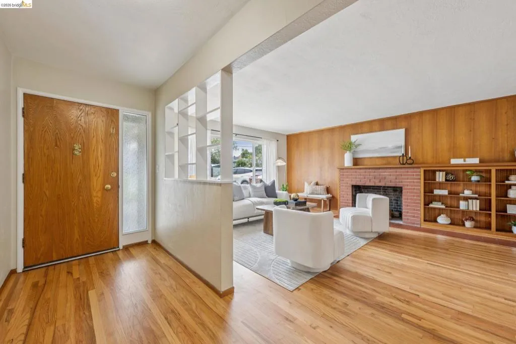 Hardwood flooring, wood paneling, brick fireplace, built-in shelving, and transom window