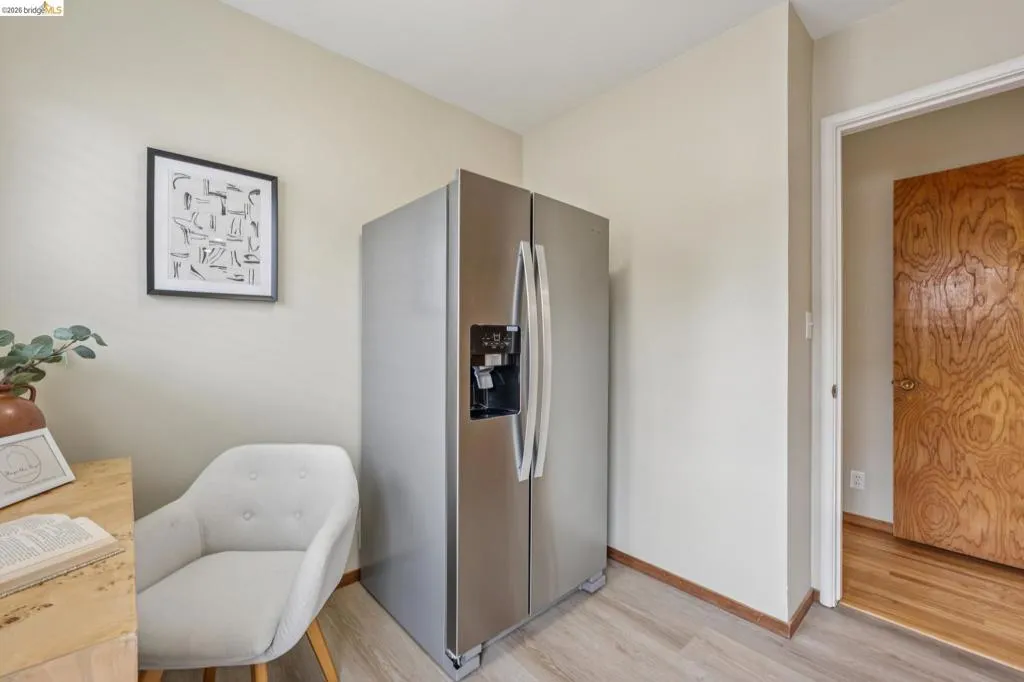Stainless steel side-by-side refrigerator, wood-finish flooring, and a light-toned wood door