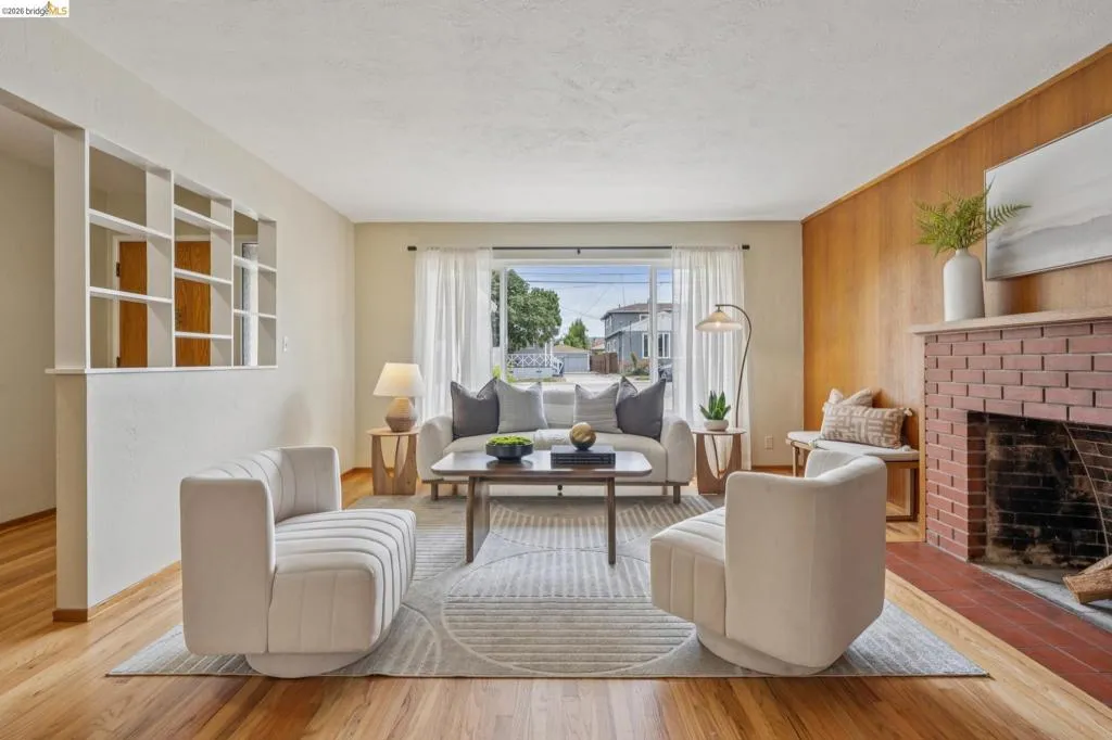 Hardwood flooring, natural wood paneling, brick fireplace, built-in shelving, and a large front-facing window
