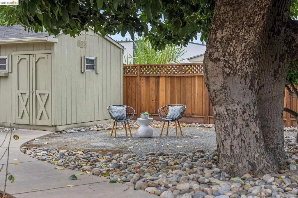 Storage shed with double doors and window accents, gravel patio, wood privacy fence with lattice top, and a concrete pathway