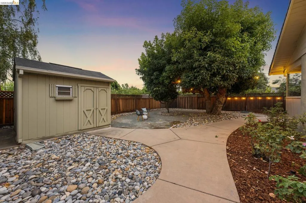 Curved concrete pathways, mature trees, wood fencing, and a detached storage shed