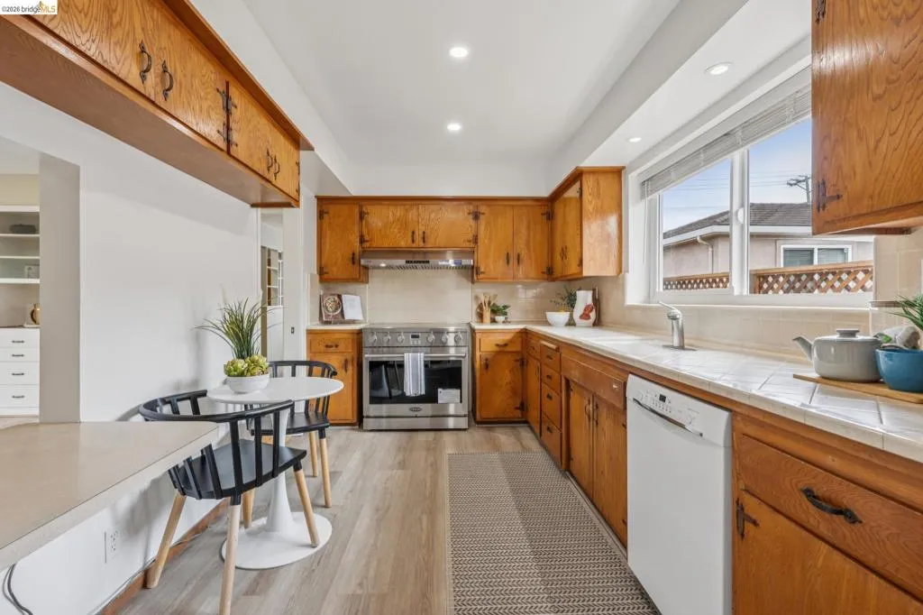 Kitchen featuring wood-finish cabinetry, stainless steel range, white dishwasher, tile countertops, and recessed lighting