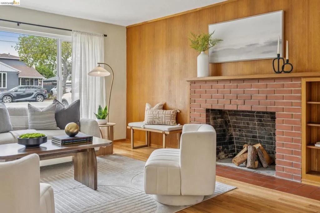 Brick fireplace with a wood mantel, wood-finish flooring, wood paneling, built-in shelving, and large windows