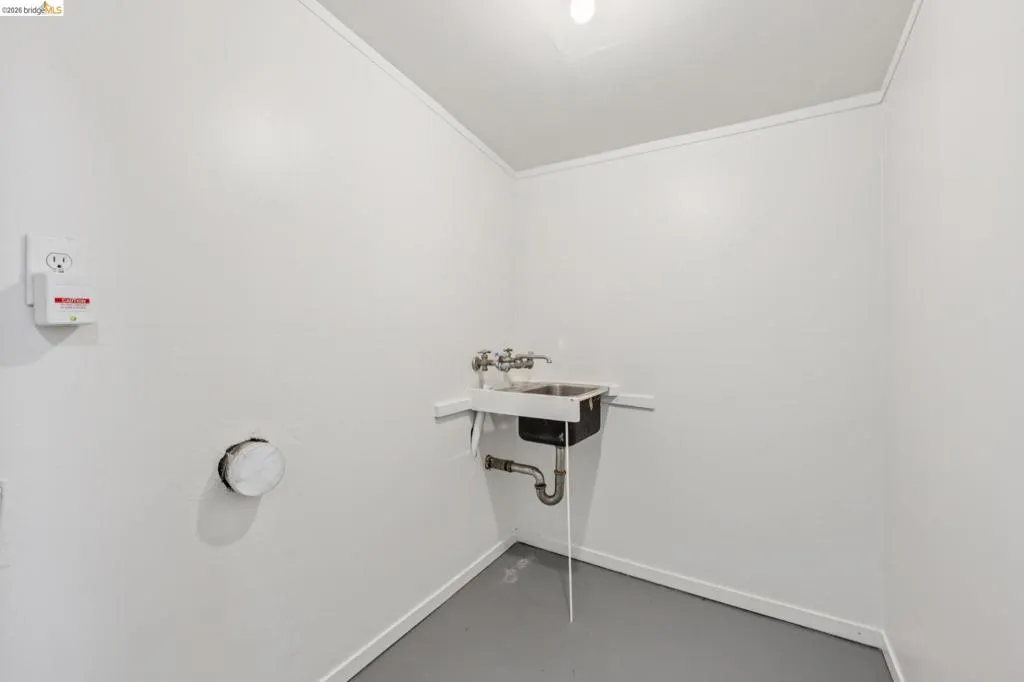 Utility sink with dual faucets, wall-mounted outlets, and gray flooring