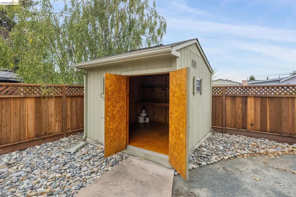 Detached storage shed with double doors, interior shelving, a concrete entry pad, and surrounding decorative river rock