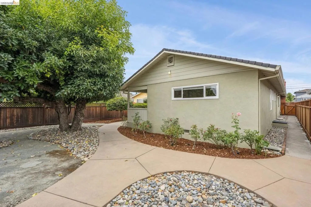 Exterior featuring a stucco finish, tiled roof, mature tree, and concrete pathway with river rock accents
