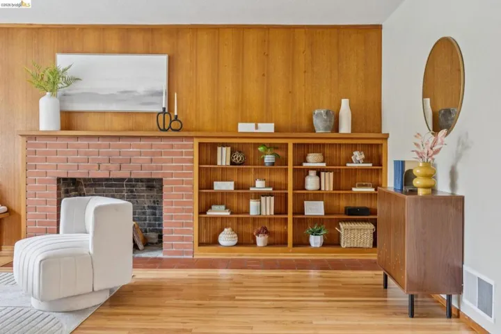 Hardwood flooring, brick fireplace with a wood mantel, built-in shelving, wood paneled wall