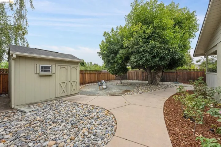 Manicured backyard with a storage shed, concrete pathways, mature trees, and a wooden fence
