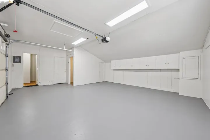 Spacious garage featuring a light gray floor, white walls, built-in white cabinetry, and overhead fluorescent lighting