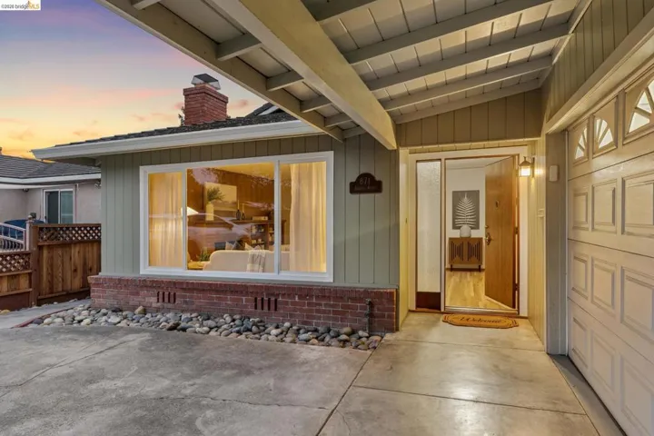 Covered entry with exposed beam ceiling, wood-finish entry door, and integrated garage access