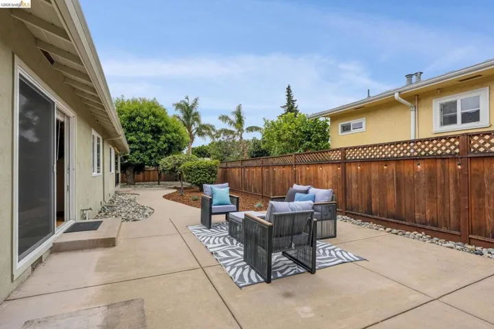Expansive concrete patio with a curved walkway, bordered by river rock landscaping, a privacy fence, and mature trees